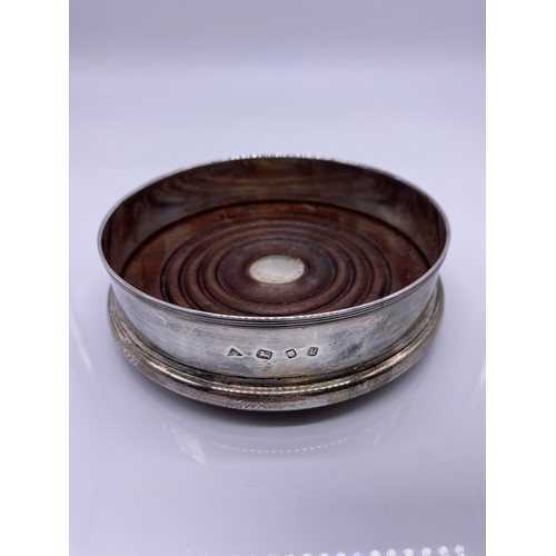 9 - A modern silver wine coaster
JAC, London 1986 of plain form threaded rim
mahogany base with silver b... 