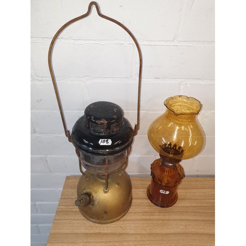 108 - A vintage Storm Lamp together with Amber Glass Oil Lamp