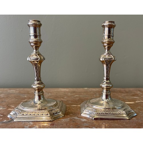 36 - A Pair of George I silver tapersticks. Each on a square base with in-curved angles, with baluster st... 