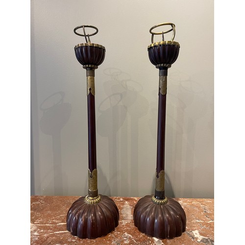 A pair of lacquered wood candlesticks (18th century), each with a large, solid hemispherical base that is carved in the form of a stylised chrysanthemum flower. A tall cylindrical stem extends from the base and is crowned by a chrysanthemum­-shaped drip pan in the form of a deep cup. This is mounted with a spike and bracket for holding a candle. The tall cylindrical stem is decorated with two foliate yellow copper mounts with chrysanthemum­-shaped finials. The mounts are engraved with leaves.