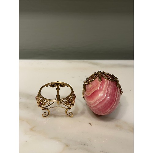 90 - A small jewelled hardstone egg on a stand in Russian taste. Banded pink hardstone. Gold setting with... 