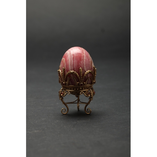 188 - Russian19th Century (?)A small jewelled hard stone egg on a standBanded pink hard stone, gold, and g... 