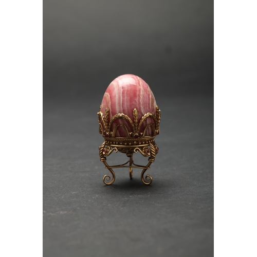 188 - Russian19th Century (?)A small jewelled hard stone egg on a standBanded pink hard stone, gold, and g... 