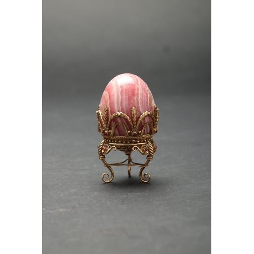 188 - Russian19th Century (?)A small jewelled hard stone egg on a standBanded pink hard stone, gold, and g... 