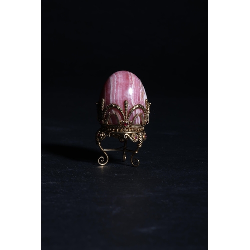 188 - Russian19th Century (?)A small jewelled hard stone egg on a standBanded pink hard stone, gold, and g... 