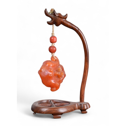 334 - Chinese19th CenturyCarnelian or orange jade pendant on a wood standProperty of a gentlemanFrom the c... 