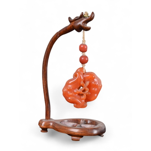 334 - Chinese19th CenturyCarnelian or orange jade pendant on a wood standProperty of a gentlemanFrom the c... 