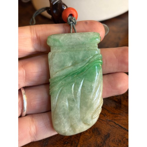 350 - Chinese20th CenturyMottled apple green coloured jadeite pendantCoral beaded topOn a wooden standProp... 