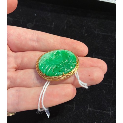 15 - A jadeite and gold brooch, circa 1950The Chinese pierced and carved apple green jadeite depicting a ... 