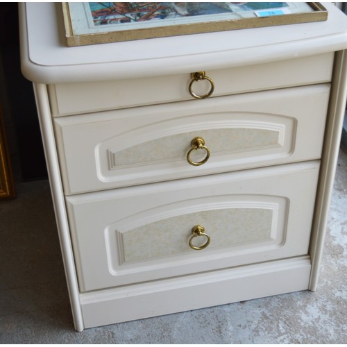 221 - A White-Finished Bedside Cabinet having Glass Covering for Top and with Brass Drop Handles