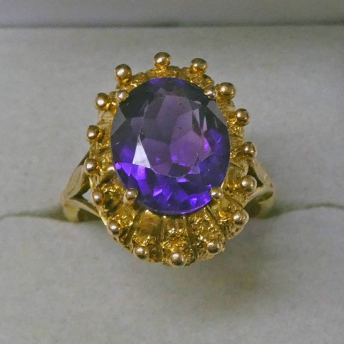 337 - 9CT GOLD AMETHYST SET RING, THE OVAL FACETED AMETHYST SET WITHIN A DECORATIVE STUDDED MOUNT - 6.1 G