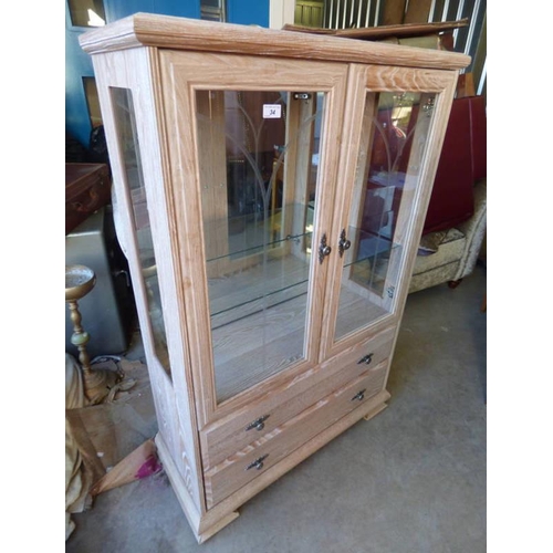 34 - LIMED OAK EFFECT DISPLAY CABINET WITH 2 GLAZED PANEL DOORS OPENING TO GLASS SHELVED INTERIOR OVER 2 ... 