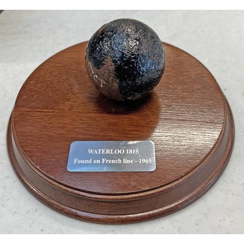 1062 - CANNON BALL ON WOODEN PLINTH, PLAQUE READS ''WATERLOO 1815 FOUND ON FRENCH LINE 1965''