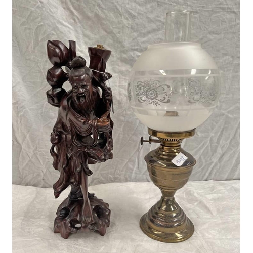 3228 - ORIENTAL CARVED WOODEN FIGURE, TABLE LAMP. HEIGHT 42 CMS, BRASS PARAFFIN LAMP WITH GLASS GLOBE SHADE