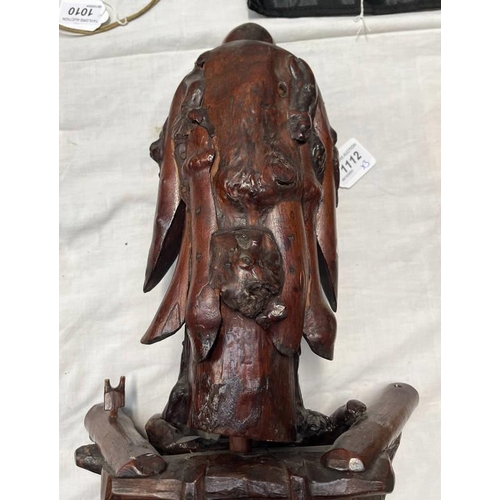 1112 - TWO CARVED WOODEN ORIENTAL FIGURES ON STANDS ALONG WTIH A CIRCULAR CAST METAL ORIENTAL PLAQUE ON STA... 