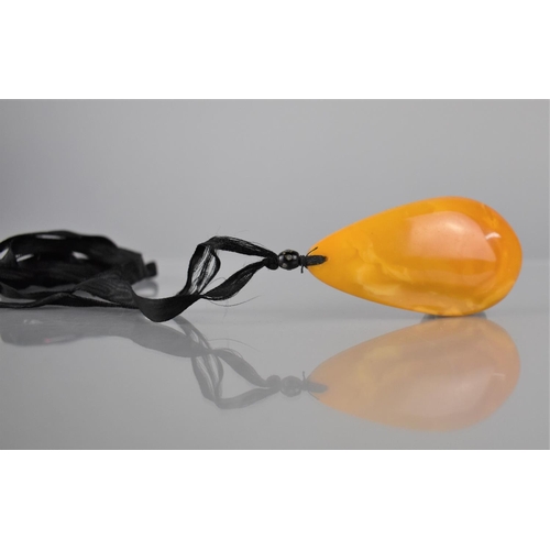 234 - A Large Egg Yolk Amber Pendant on Black Silk Ribbon, Possibly 19th Century, Pear Shaped Pendant Meas... 