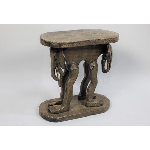 77 - An African Carved Wooden Souvenir Stool, the Supports in the Form of Elephant with Human Legs, Oval ... 