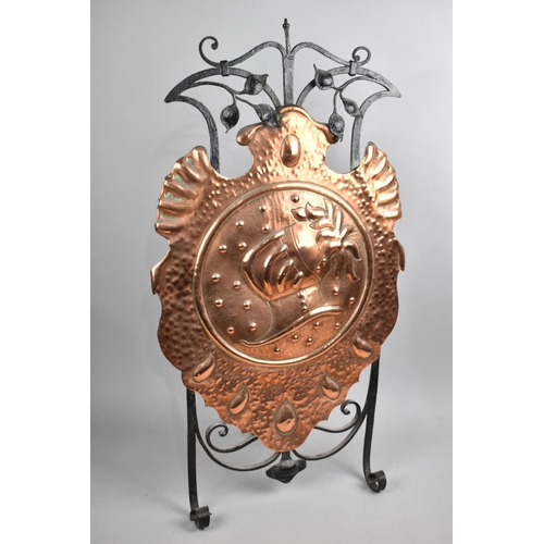 127 - An Arts and Crafts Wrought Iron and Copper Fire Screen, Shield Shaped Copper Panel Decorated with He... 