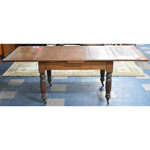 545 - An Edwardian Oak Drawer Leaf Dining Table On Turned Reeded Supports Culminating in Casters, Extends ... 