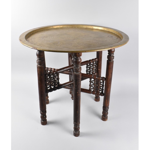 75 - An Engraved Brass Benaries Tray on Folding Wooden Stand, 56.5cms Diameter, Islamic Decoration to Top