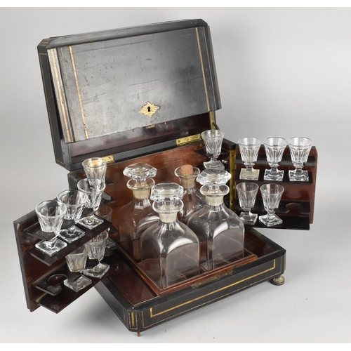 A 19th Century Coromandel Fitted Decanter Box with Hinged Top and Front Flanked by Carrying Handles Enclosing Four Decanters, Flanking Shelved Sides Housing Fourteen Drinking Glasses Having Facet Cut Bowls to Square Bases, the Coromandel Box with Brass Stringing and Fittings Raised on Brass Feet (Missing One Foot), 32x23x27cms High (In Need of Some Restoration)