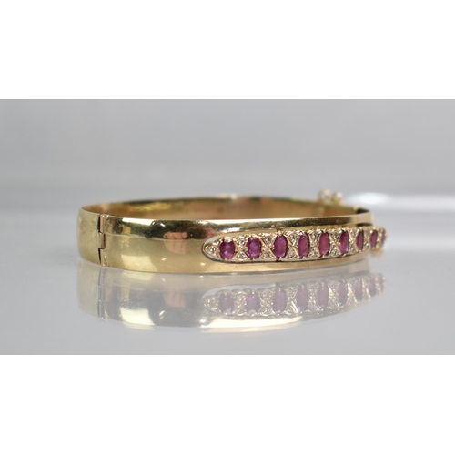 12 - A Ruby and Diamond Set 9ct Gold Hinged Bangle, Nine Graduated Oval Cut Rubies, Largest 5.1mm by 2.8m... 