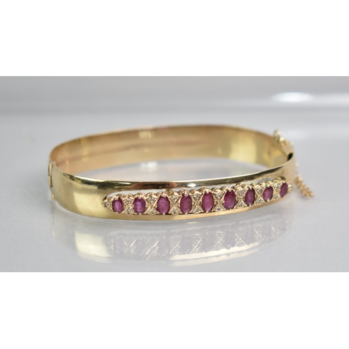 12 - A Ruby and Diamond Set 9ct Gold Hinged Bangle, Nine Graduated Oval Cut Rubies, Largest 5.1mm by 2.8m... 