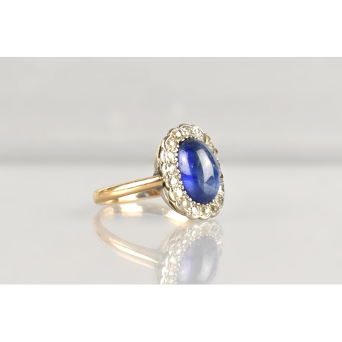 An Early 20th Century Sapphire, Diamond and 18ct Gold Ring, Central Cabochon Stone Measuring 6.8mm by 10.1mm Approx, Milgrain Set in White Metal and with Halo of Eighteen Small Round Cut Diamonds, Similarly Set, Polished D Shape Band Stamped to the Interior 18ct, Sapphire Bright and with Chatoyancy/Cats Eye Form observed in the South West Corner, Size N, 3.7gms