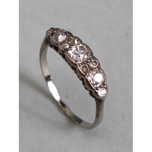 70a - Unmarked white Gold Diamond ring set with nine diamonds, the largest central diamond flanked by a pa... 