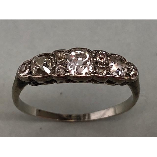 70a - Unmarked white Gold Diamond ring set with nine diamonds, the largest central diamond flanked by a pa... 