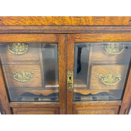 413 - Antique Smokers cabinet, in light oak, part glazed doors opening to show drawers and pipe rack  appr... 