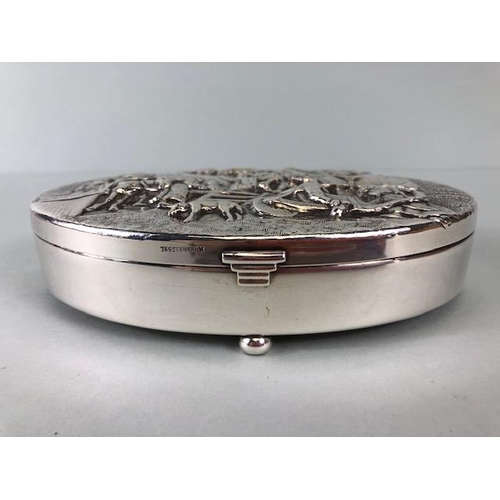 92 - Danish white metal toilet or trinket box, oval shape on bun feet the lid embossed with a drunken vil... 