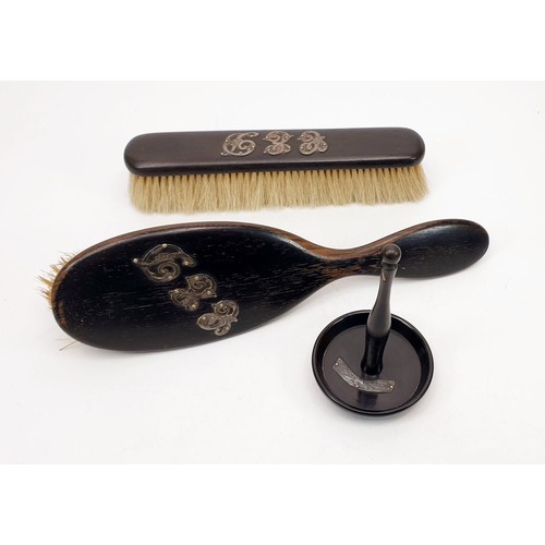 138 - An ebony ring holder with a hallmarked silver mount together with two brushes with white metal mount... 