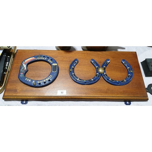 53 - Three horse shoes decorated with Guinness, pints and a toucan, mounted on a board, width 24.75