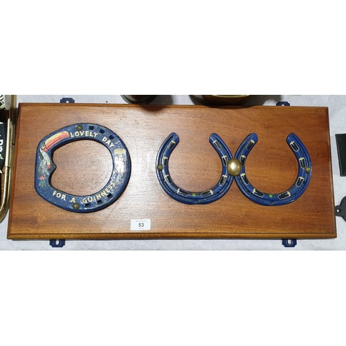 53 - Three horse shoes decorated with Guinness, pints and a toucan, mounted on a board, width 24.75