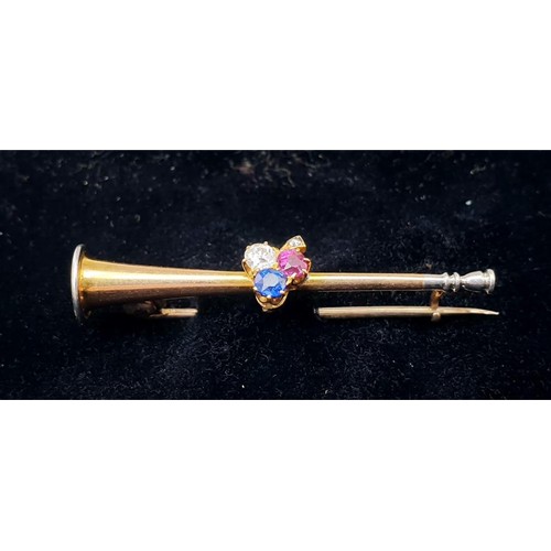 18 - A yellow metal brooch in the form of a trumpet set with diamond, sapphire and ruby, length 1.75