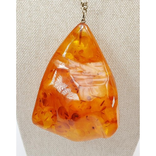 21 - A large amber pendant with butterscotch inclusions, pendant length 8.5cm, on a silver plated chain, ... 