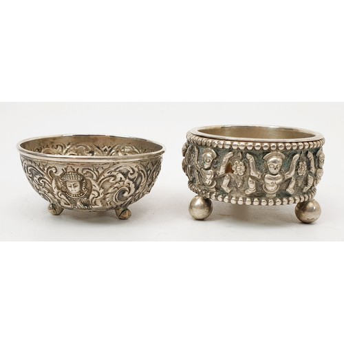 57 - Two far eastern white metal condiment type bowls each embossed with deities and foliage, the largest... 