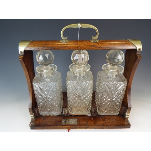 586 - Early 20th Century Oak and brass tantalus, Original matching pressed glass decanters. Key present.