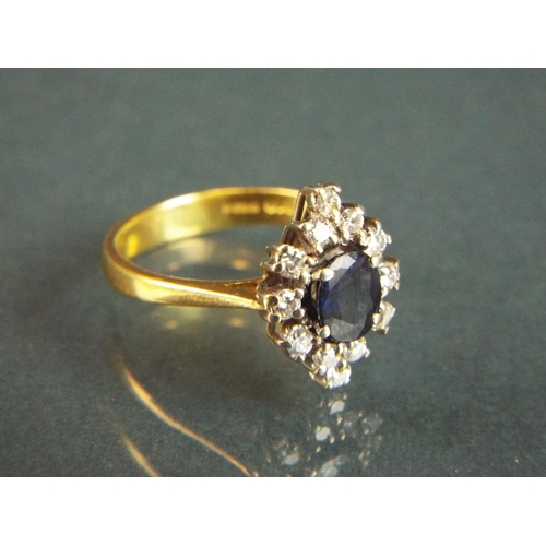 63 - 18ct Yellow Gold ring set with a central Sapphire with Diamond Surround.  Finger size 'M'   3.6g