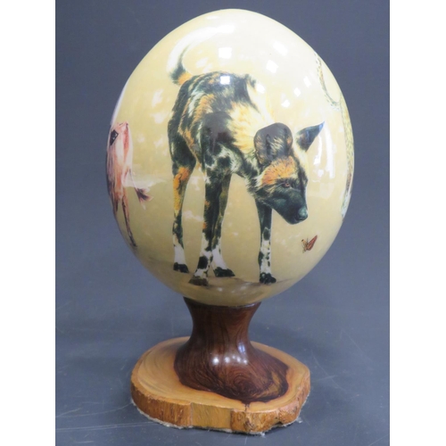 375 - Beautifully decorated Ostrich Egg supported by a hand carved piece of African Hardwood. Egg is decor... 