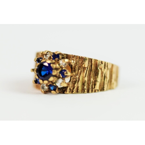 209 - 9ct Yellow Gold ring with textured bark effect to shank. Set with synthetic Sapphire in a flower pat... 