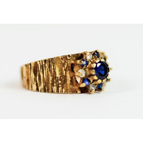 209 - 9ct Yellow Gold ring with textured bark effect to shank. Set with synthetic Sapphire in a flower pat... 