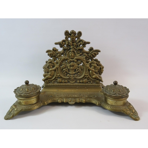 580 - Ornate brass desk tidy with inkwells and letter rack decorated with cherubs (1 glass liner missing).... 