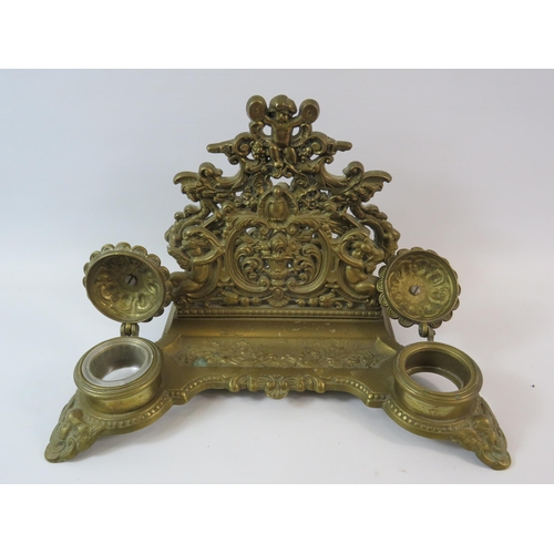 580 - Ornate brass desk tidy with inkwells and letter rack decorated with cherubs (1 glass liner missing).... 