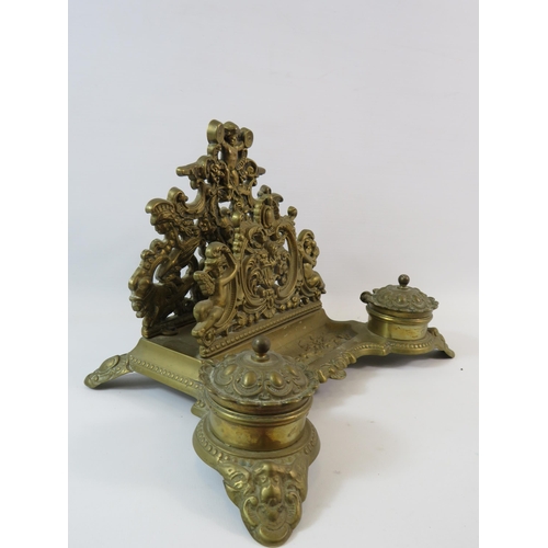 580 - Ornate brass desk tidy with inkwells and letter rack decorated with cherubs (1 glass liner missing).... 