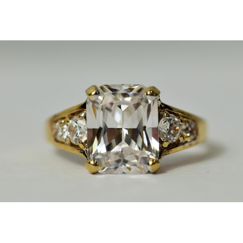 222 - 9ct Yellow Gold ring set with a large Emerald Cut CZ Gemstone accompanied by smaller Brilliant cut s... 