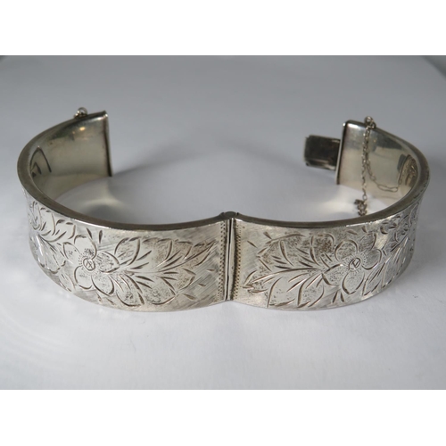 536 - 925 Hallmarked sterling silver bangle. Inscribed flowers to both sides. Safety chain fitted to nip u... 