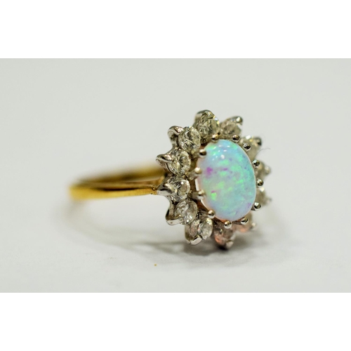 327 - 9ct Yellow Gold ring set with a lovely Central Opal which measures 8 x 5mm, surrounded by Clear gems... 