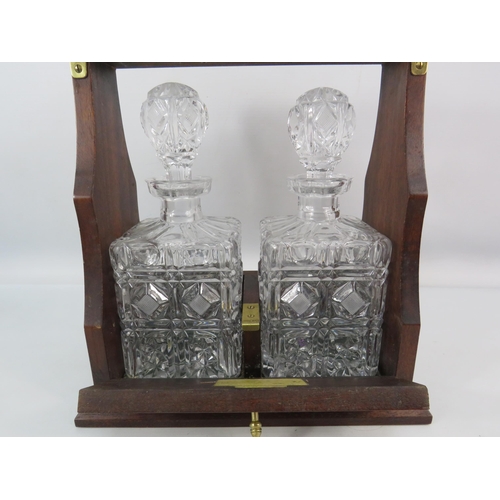 719 - Oak two decanter Tantalus with brass fittings and 2 cut glass decanters.